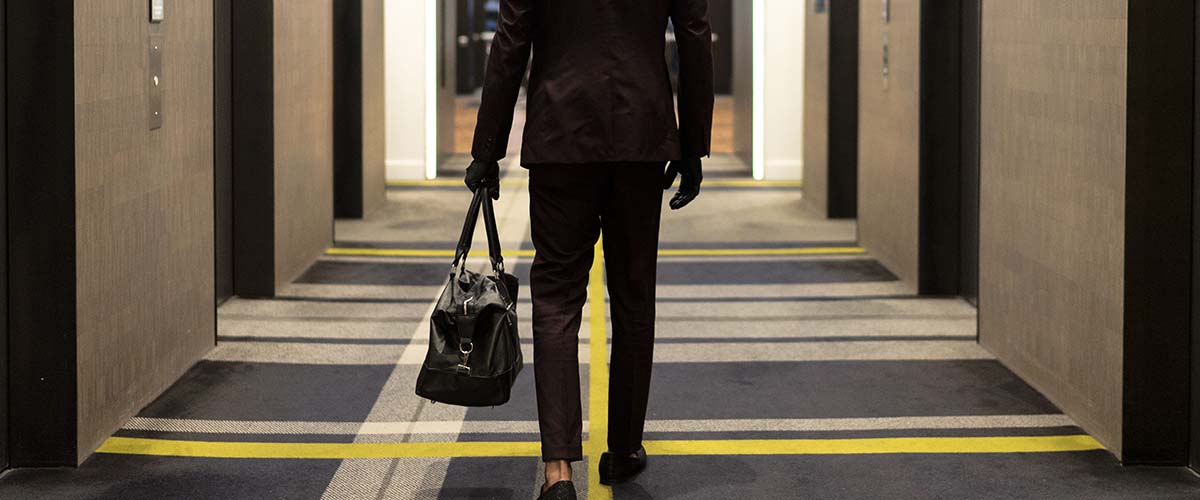 ¿Puedo demandar al hotel por mis lesiones? 3 tall man in a suit walks towards hotel elevators with a duffle bag SBI 346274260 1